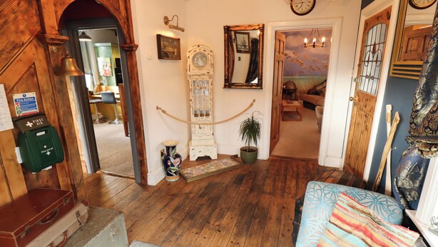 Una habitación con escalera de madera, un reloj antiguo, un espejo y un sofá con un cojín estampado.