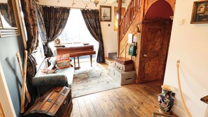 Una habitación con una escalera de madera, un piano y un banco con maletas.