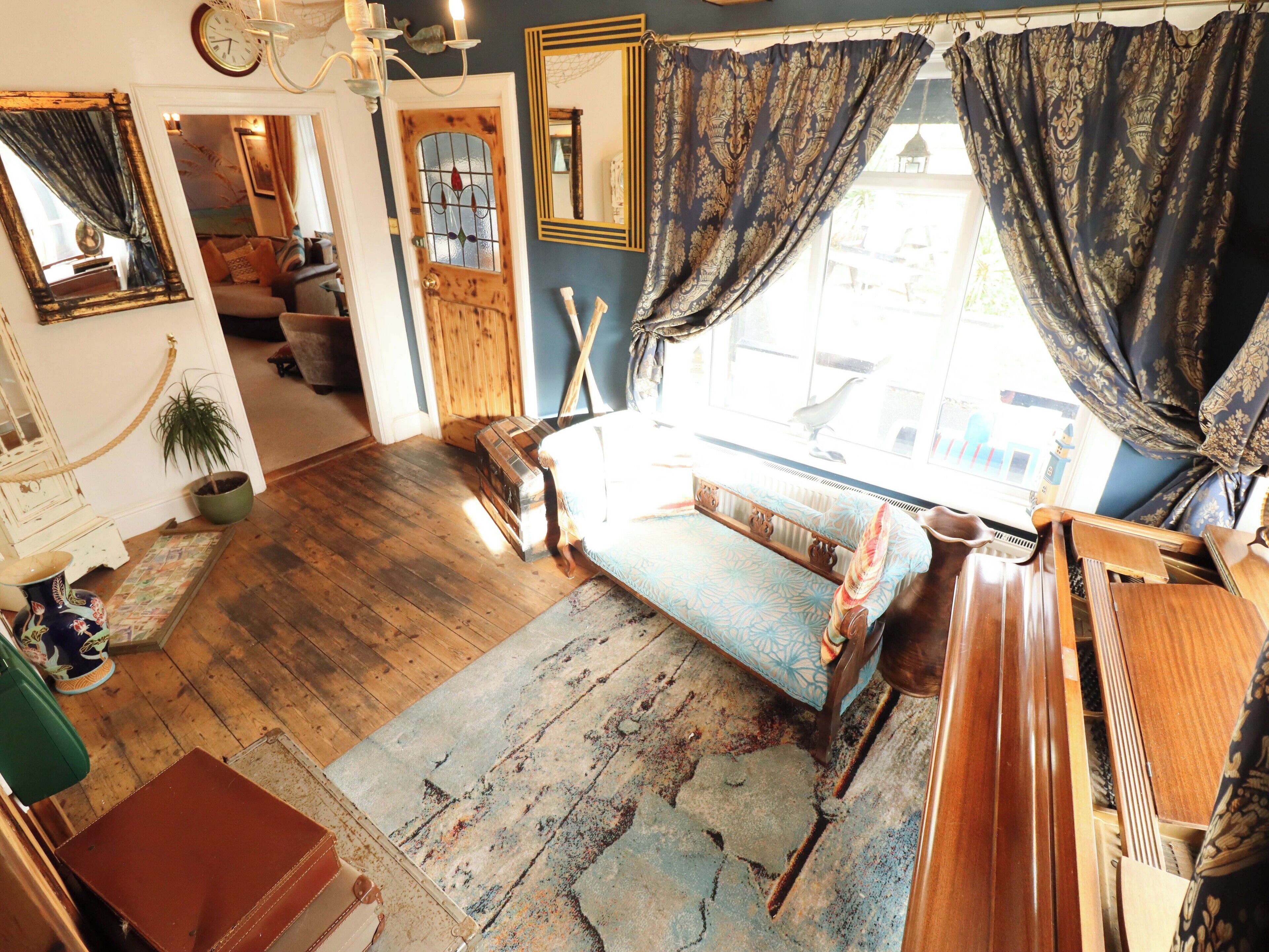 A room with a wooden floor, a sofa, a window with curtains, a mirror, and a door with a glass panel.