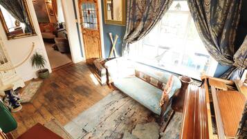 A room with a wooden floor, a sofa, a window with curtains, a mirror, and a door with a glass panel.
