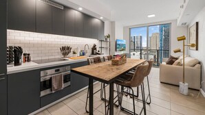Een moderne keuken met donkere kastjes, een wit aanrechtblad en een eethoek met een houten tafel en stoelen.