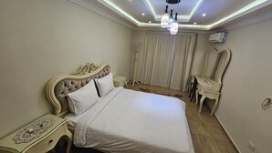 Un dormitorio ordenado con una cama grande, una mesita de noche, una silla y una lámpara en el techo.