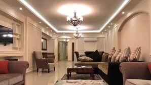 Amplia sala de estar con una gran televisión de pantalla plana montada en la pared, un candelabro y varias zonas de estar con sofás y sillones.