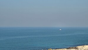 Vista costera con un barco a lo lejos, costa rocosa y cielo despejado.