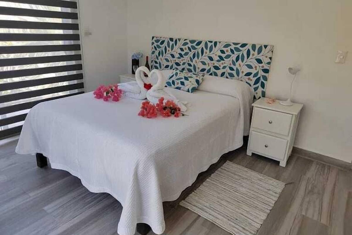 A neatly made bed with a white bedspread, two swan-shaped pillows, and pink floral arrangements.