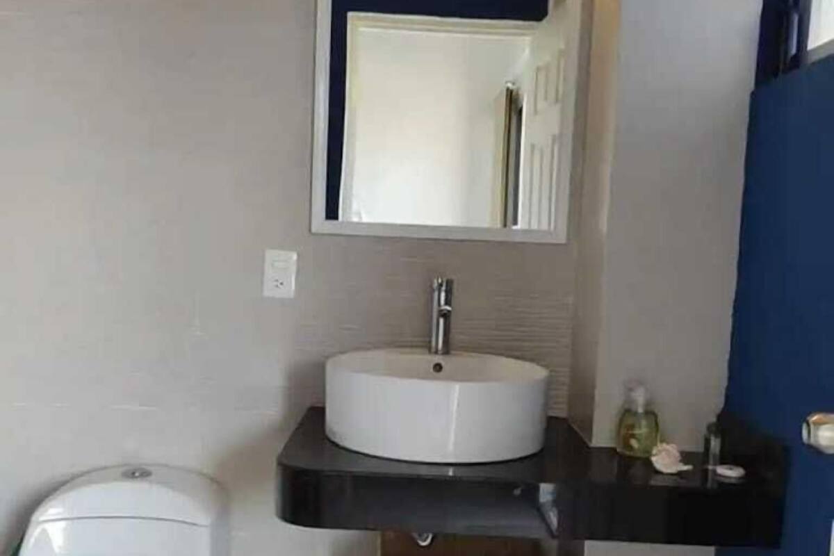 A bathroom with a white toilet, a white sink with a black countertop, and a mirror above the sink. There is a small wooden box under the countertop.