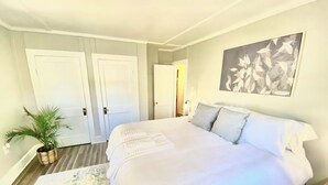 A bedroom with a large bed, a potted plant, and a framed artwork on the wall. - The Little Sandpiper - Charming Port Royal Cottage (Port Royal)