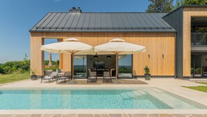 Ein modernes Haus mit Schwimmbad, Sitzgelegenheiten im Freien und einem großen Fernsehbildschirm.