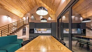 A spacious dining area with a long wooden table and modern chairs, a teal sofa, and a staircase leading to an upper level. - Blacksmith House - Stylish vacation home with spa & nature views (Varaždinske Toplice)