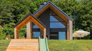 A modern house with a wooden deck, a green slide, and a large glass window. - Blacksmith House - Stylish vacation home with spa & nature views (Varaždinske Toplice)