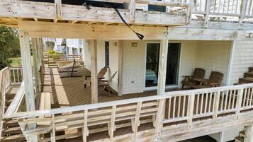 Una terraza de madera con un área de descanso cubierta, una hamaca y una puerta corrediza de vidrio que da a una habitación.