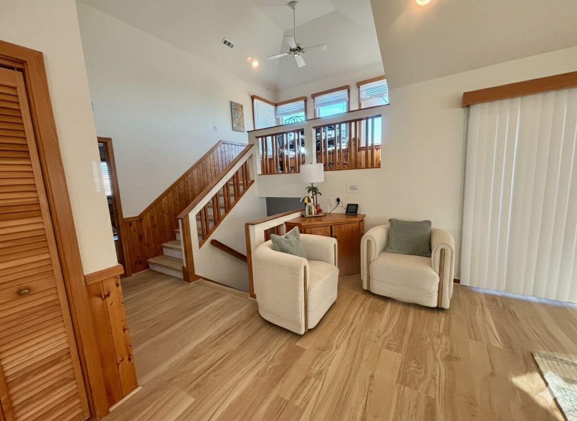 Un vaste espace de vie agrémenté d’un escalier en bois, de deux fauteuils, d’une petite table et d’un ventilateur de plafond.