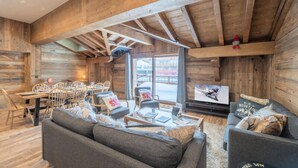L’intérieur d’un chalet confortable, avec un canapé, des fauteuils, une table à manger et un téléviseur.