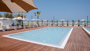 Area piscina con lettini e ombrelloni, un solarium in legno e vista sul mare.