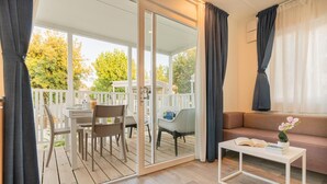 Un'accogliente area soggiorno con una porta scorrevole in vetro che dà su un patio, un divano bianco, un tavolino con un libro e un fiore, e un set da pranzo.