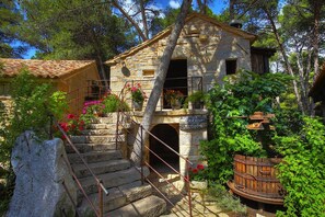 Ein rustikales Steinhaus mit Ziegeldach, einer Treppe, die zu einem Balkon führt, und einer Brunnen aus Holzfässern.