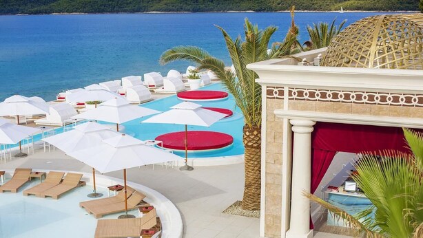A pool area with sun loungers and umbrellas, a palm tree, and a view of the sea. - Amadria Park Sibenik Apartment 4+3 for 7 persons (Sibenik)