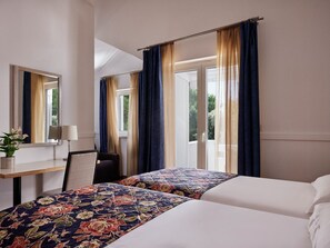 Ett hotellrum med två sängar, ett skrivbord med en lampa, en spegel och ett fönster med gardiner.