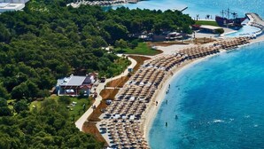 An aerial view of a coastal area with a long beach lined with umbrellas and a small boat dock. - Amadria Park Sibenik Apartment 4+3 for 7 persons (Sibenik)