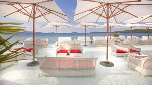 A beachside lounge area with white wicker furniture and umbrellas, overlooking the sea.