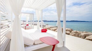 A beachside lounge with white canopies, a red table, and a view of the sea. - Amadria Park Sibenik Beach Villa for 7 persons (Sibenik)