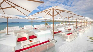 A sunlit outdoor seating area with white wicker furniture and red cushions, overlooking a clear blue sea. - Amadria Park Sibenik Apartment 2+2 with sea view for 4 persons (Sibenik)