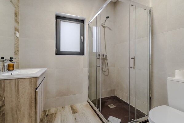 Un baño moderno con cabina de ducha de vidrio, lavamanos con tocador de madera y un inodoro.