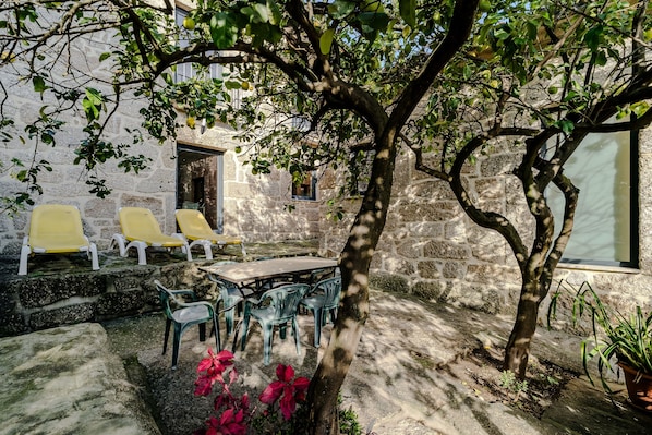 Un bâtiment en pierre doté d’une cour, d’un espace extérieur aménagé pour s’asseoir et d’un arbre.