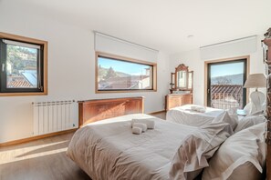 Een slaapkamer met twee bedden, een houten hoofdbord, een dressoir, een spiegel en uitzicht op buiten.