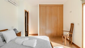 A bedroom with a bed, a wooden wardrobe, a chair, and a desk with a lamp. - Holiday Home 'Casa Feixa Gerês' with Mountain View, Wi-Fi & Air Conditioning (Gerês)