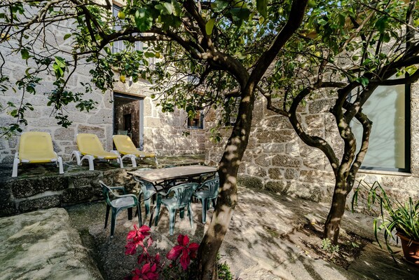 A stone building with a courtyard, outdoor seating, and a tree.