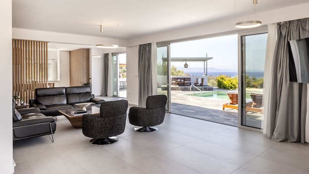 A modern living room with a sofa, armchairs, and a coffee table. There is a large sliding glass door leading to a pool area. - Luna Mare in Agia Marina Chrysochous (Ayia Marina Chrysochous)