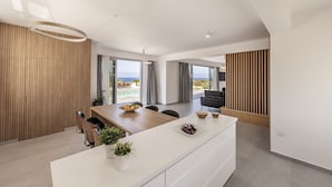 A modern interior with a dining area, kitchen, and living space, featuring large windows and a view of the sea. - Luna Mare in Agia Marina Chrysochous (Ayia Marina Chrysochous)