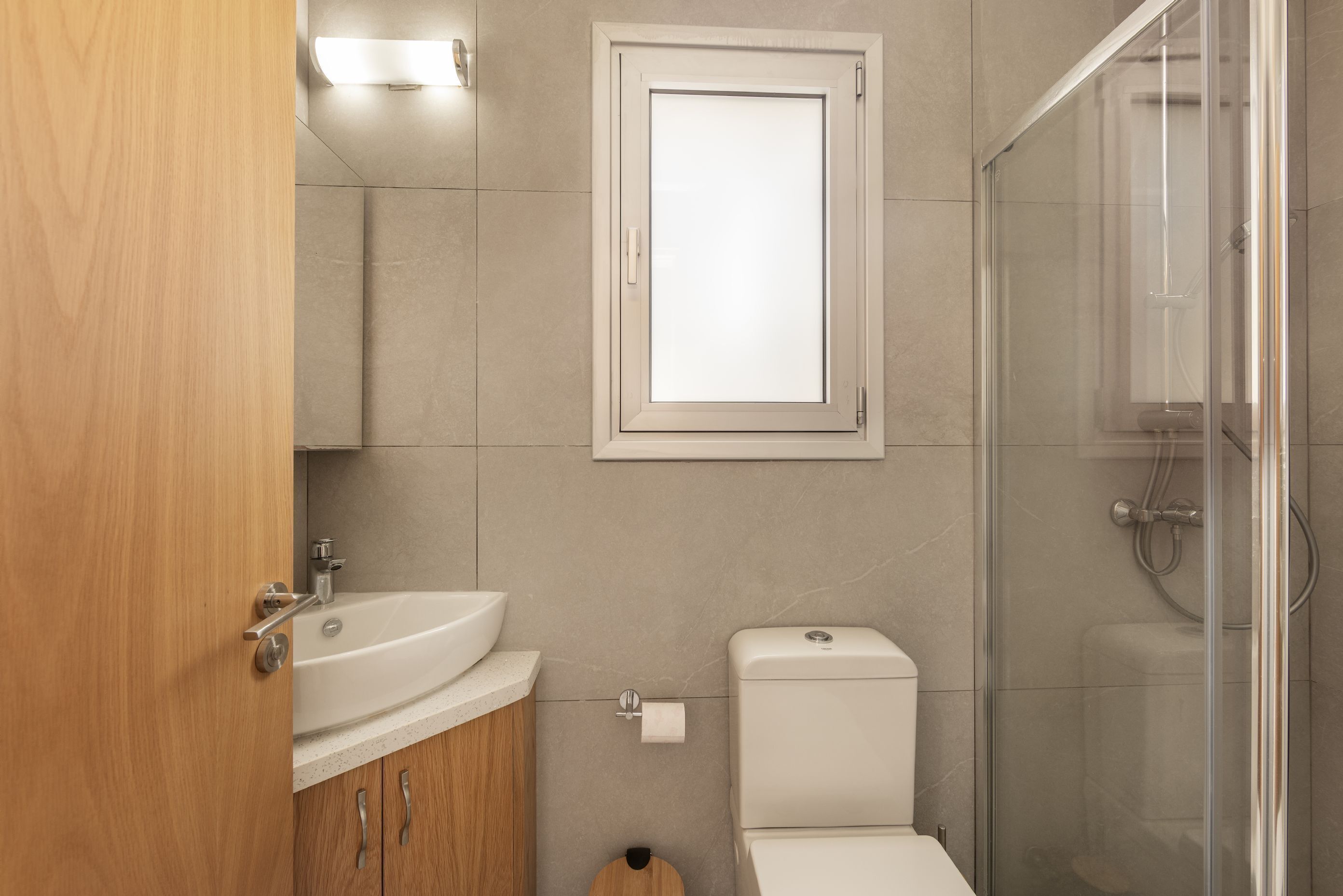 A modern bathroom with a wooden vanity, a white sink, a toilet, and a glass shower enclosure.