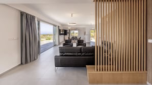 A modern living room with a black sofa, a wooden partition, and a view of the outdoors. - Luna Mare in Agia Marina Chrysochous (Ayia Marina Chrysochous)