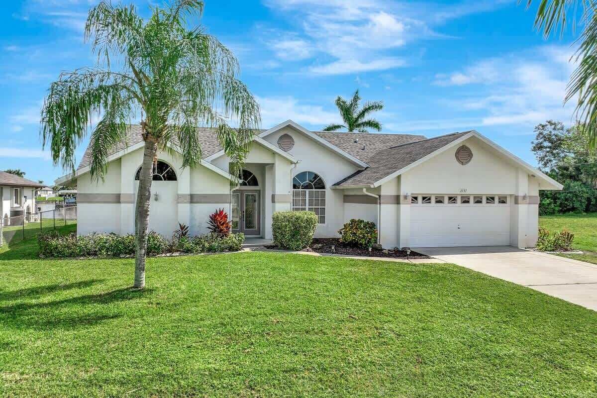 A single-story house with a front garage, a well-maintained lawn, and a palm tree.