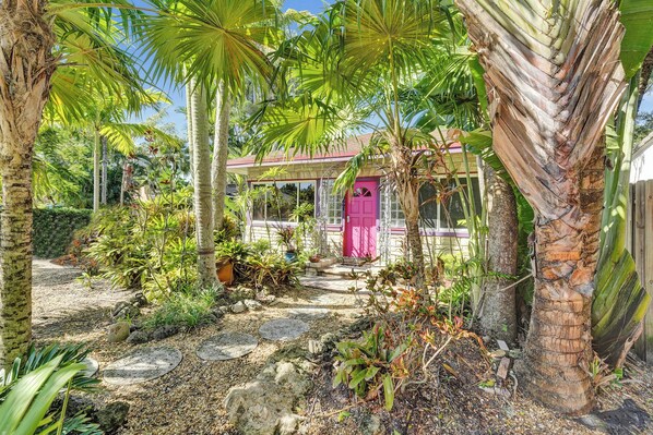 A tropical garden with a pink house, palm trees, and a stone pathway.