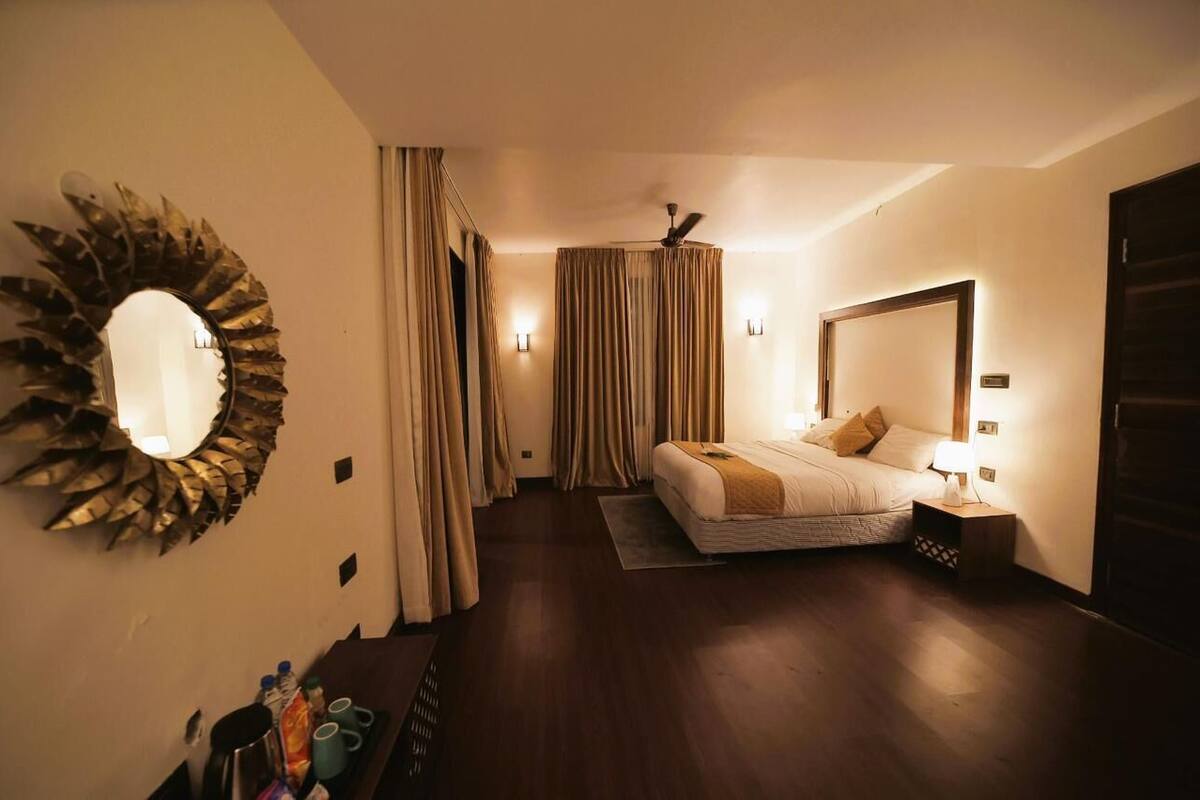 Een hotelkamer met een bed, nachtkastje, lamp, gordijnen en een spiegel aan de muur.