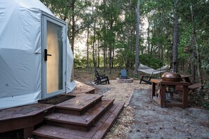 A tent with a door, a grill, and a fire pit in a wooded area.