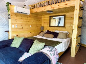 A cozy wooden room with a bunk bed, a bedside table, a mirror, and string lights.