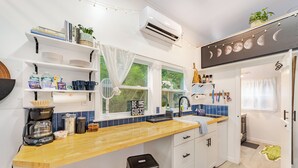 Una cucina moderna con mobili bianchi, un piano di lavoro in legno e un forno integrato. Sono presenti sgabelli da bar, una macchina da caffè e una finestra con tende.