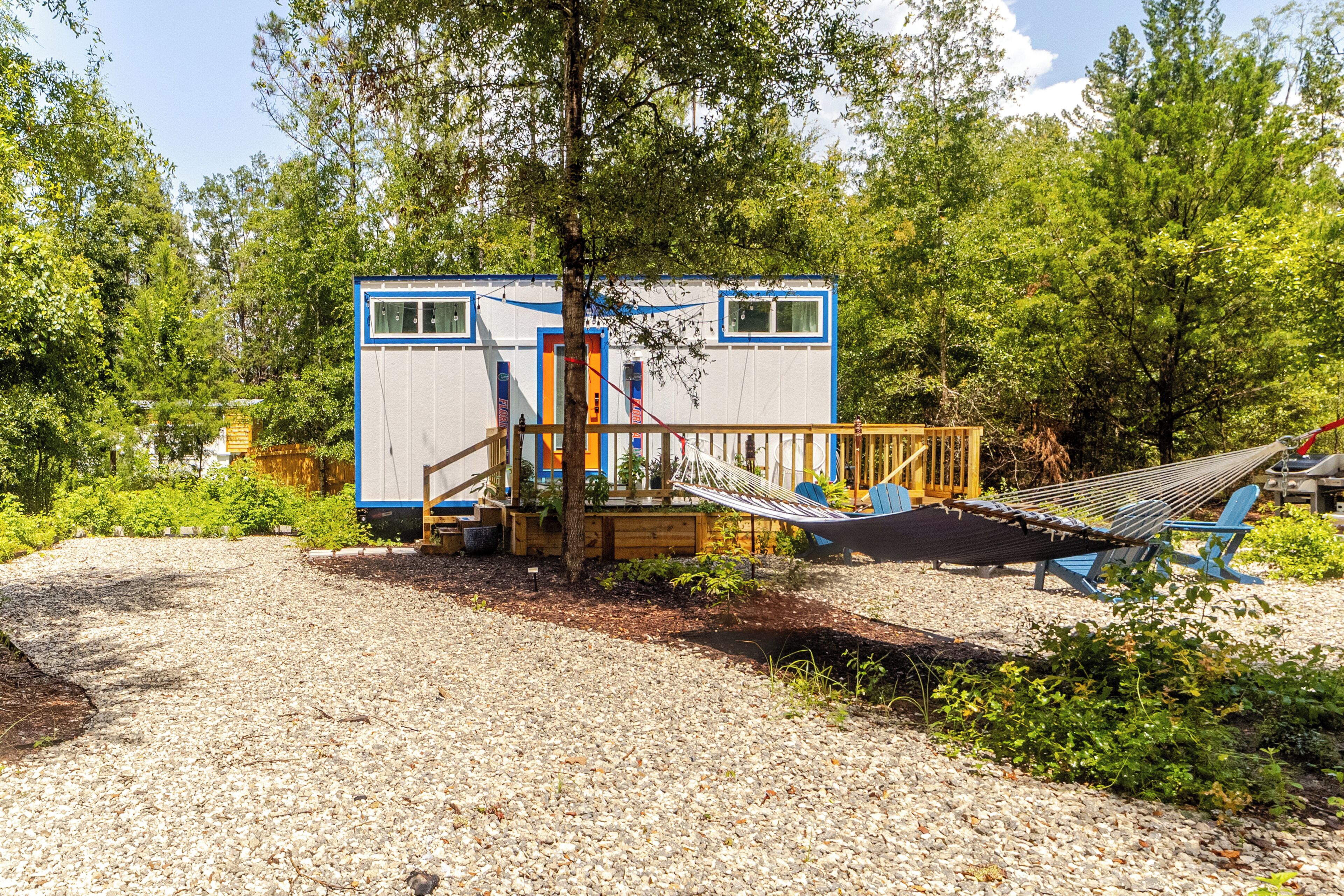 A small cabin with a deck and hammock, surrounded by trees and gravel.