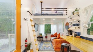 Un appartamento moderno e compatto con una zona notte soppalcata, angolo cottura e soggiorno con divano e tavolo da pranzo.