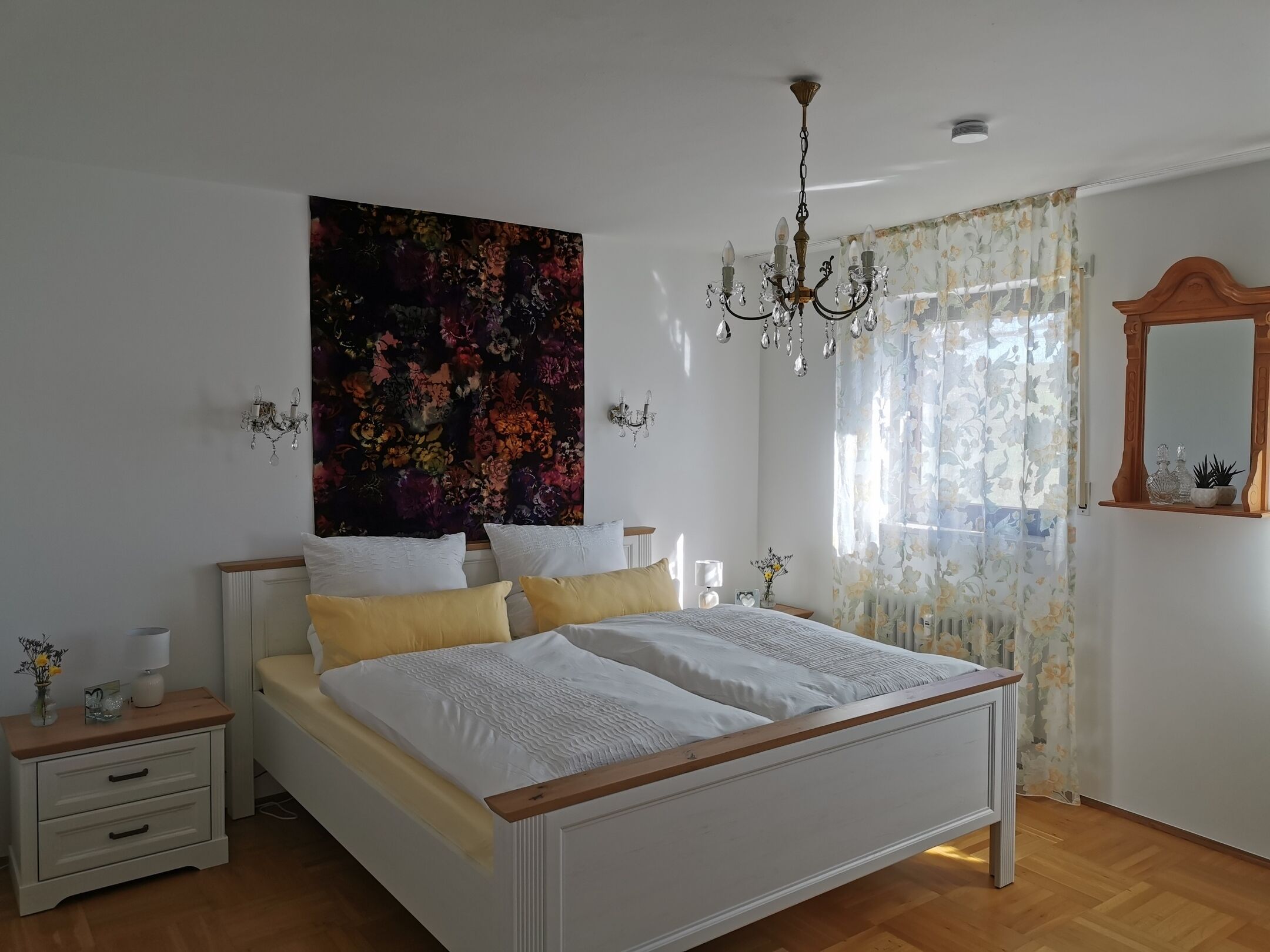 Ein Schlafzimmer mit einem großen Bett, einer Kandelaber, floralen Vorhängen und einem Wandteppich mit Blumenmuster.