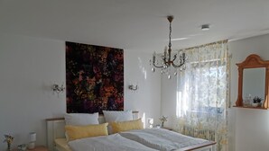 A bedroom with a large bed, a chandelier, floral curtains, and a floral wall tapestry. - Vacation apartment "Fröhlich am Baderbichl" (Tutzing)