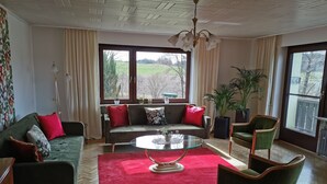 A living room with a sofa, armchairs, a glass coffee table, and a large window with curtains. - Vacation apartment "Fröhlich am Baderbichl" (Tutzing)