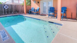 A swimming pool with a lifebuoy, a wooden fence, and blue chairs.