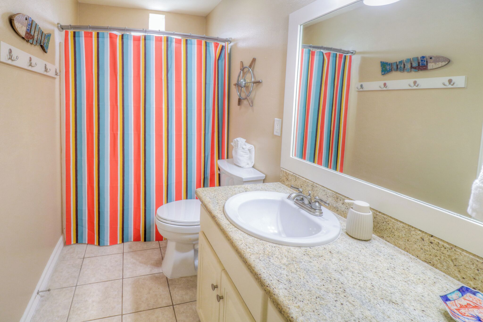 A bathroom with a striped shower curtain, a white toilet, a granite sink, and a ship-themed decoration on the wall.