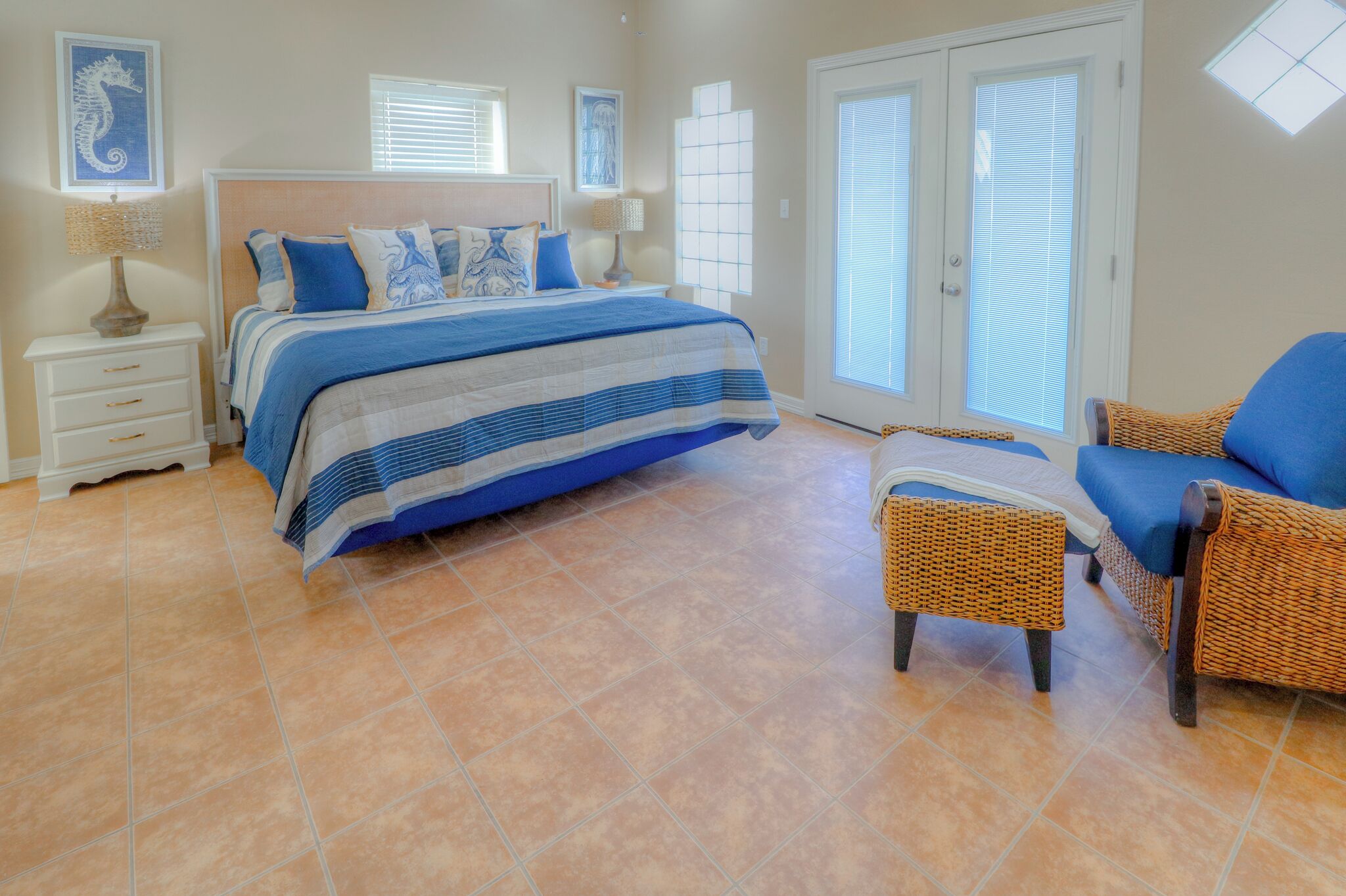 A bedroom with a bed, two nightstands, a wicker chair, and a large window with blinds.