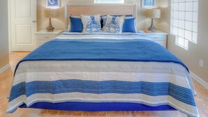 A bedroom with a large bed, two nightstands, a door, and a window with blinds.